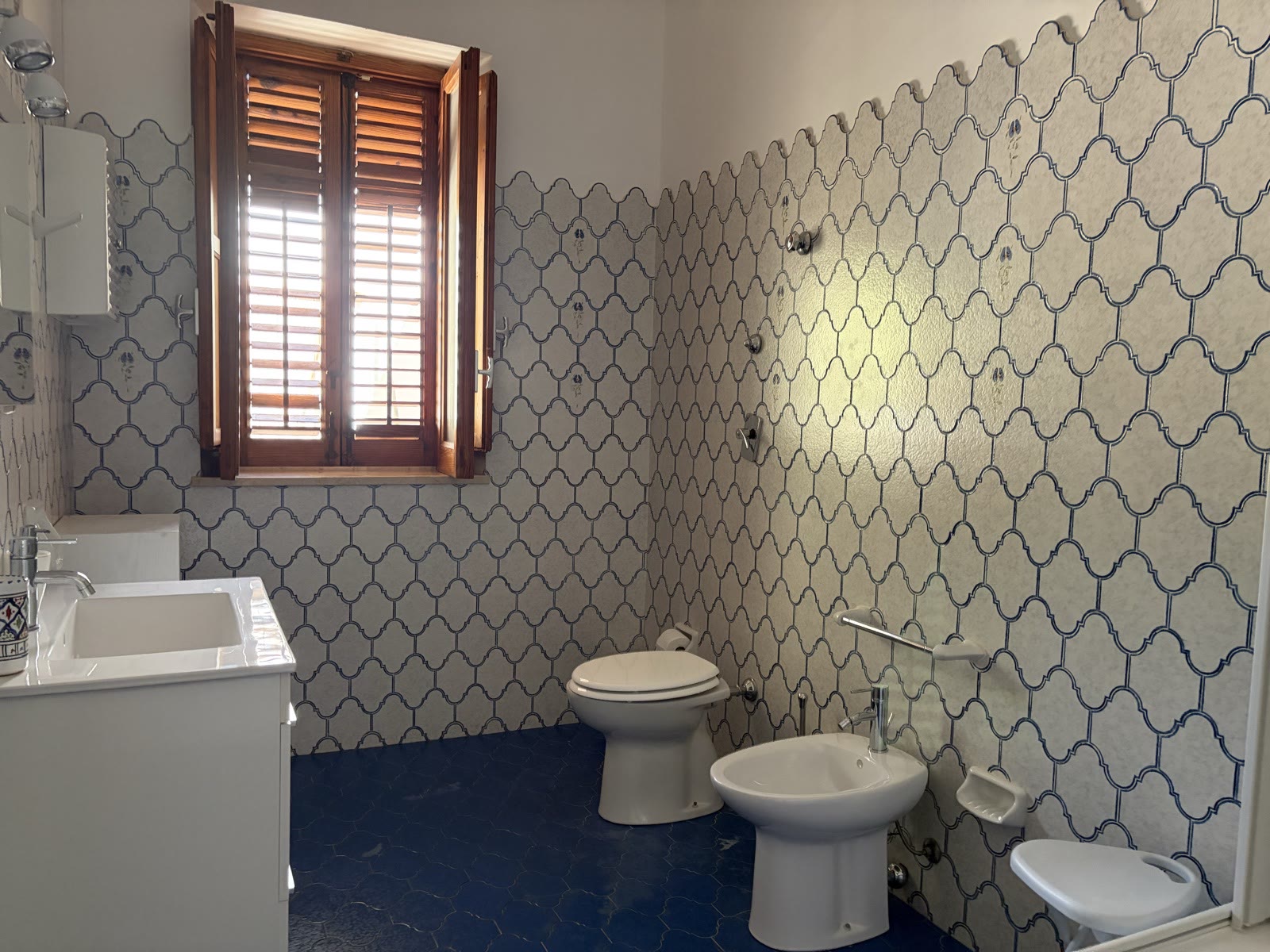 Bathroom with an azure scalloped tiled wall, blue floor and shuttered window