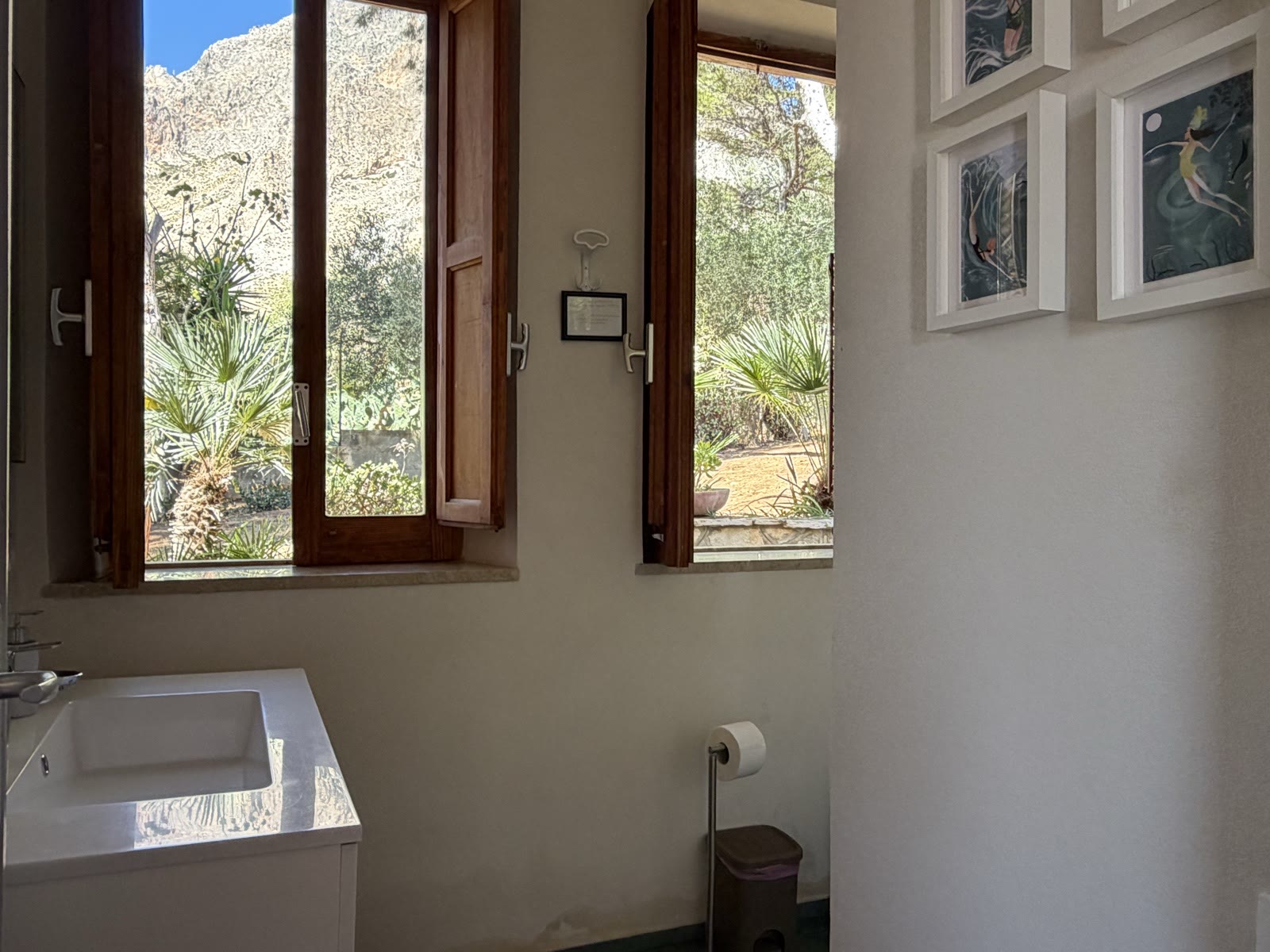 Second bathroom with washbasin and two wooden windows facing the palms and the rock face