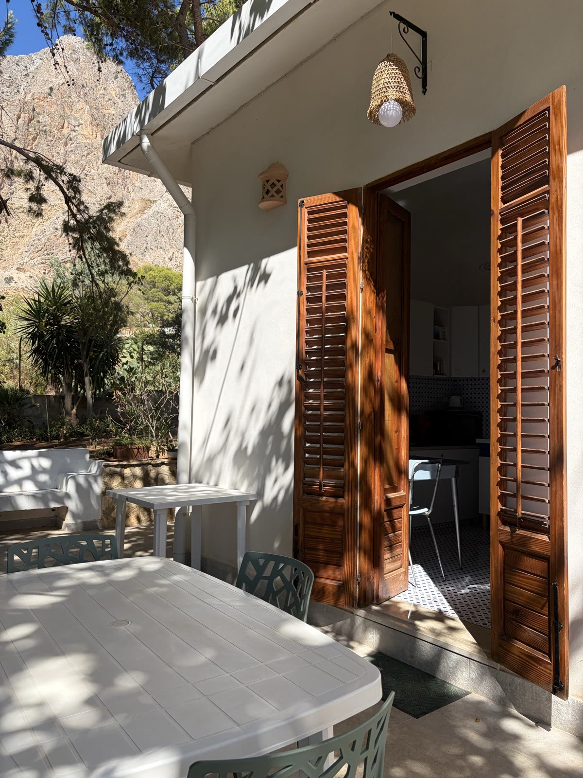 Table in the shade on the terrace, outside the kitchen French door with its shutters open